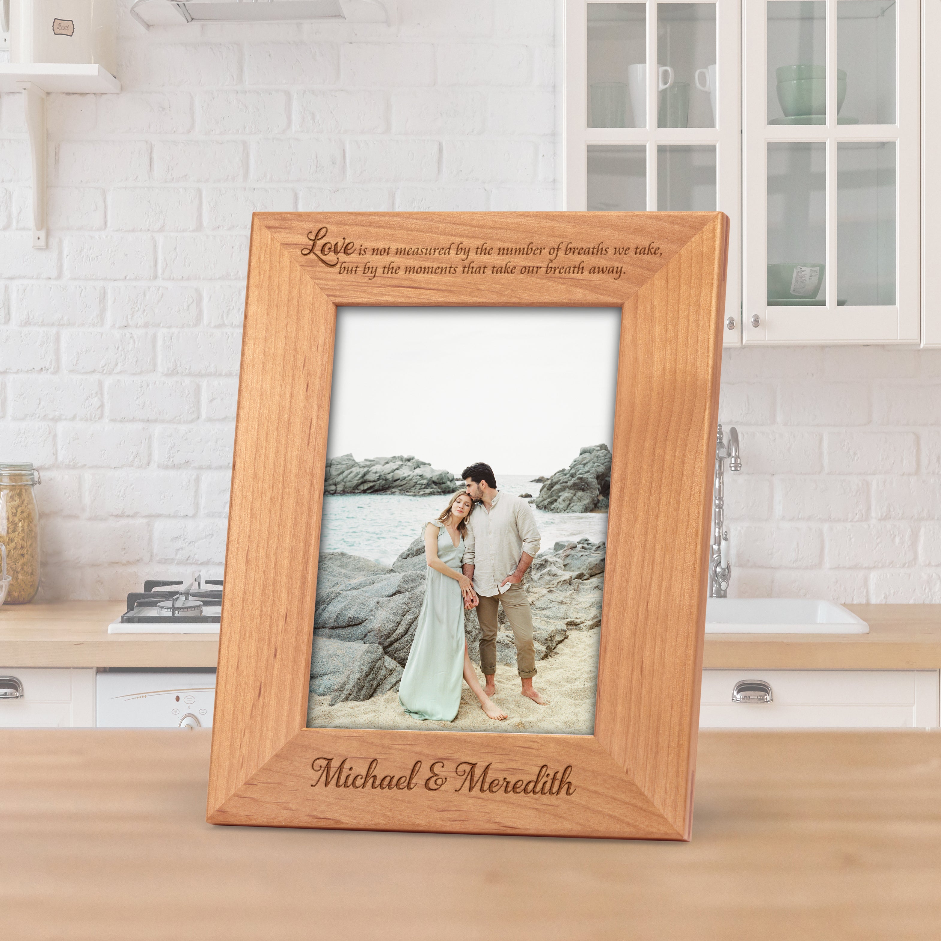 A portrait-style alder wood picture frame engraved with the words, "Love Is Not Measured by the Number of Breaths We Take, but by the Moments That Take Our Breath Away" at the top. The bottom of the frame is engraved with a couple's names.